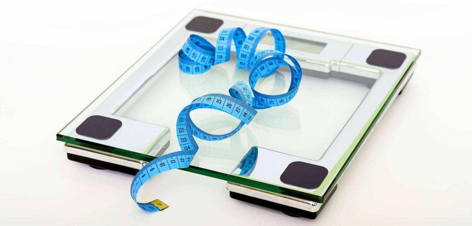A digital glass weighing scale with a blue measuring tape, symbolizing weight management.
