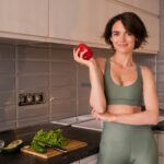 a woman standing in a kitchen holding an apple