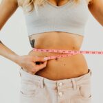 Close-up of woman in sports bra measuring waist with pink tape for fitness goals.