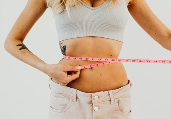 Close-up of woman in sports bra measuring waist with pink tape for fitness goals.