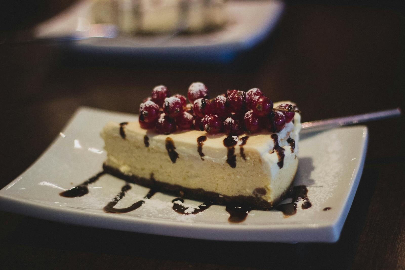 Slice of cheesecake topped with berries and chocolate drizzle on a plate.
