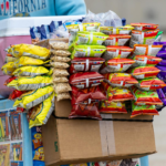 A street vendor's cart filled with a variety of colorful snack packets for sale outdoors.