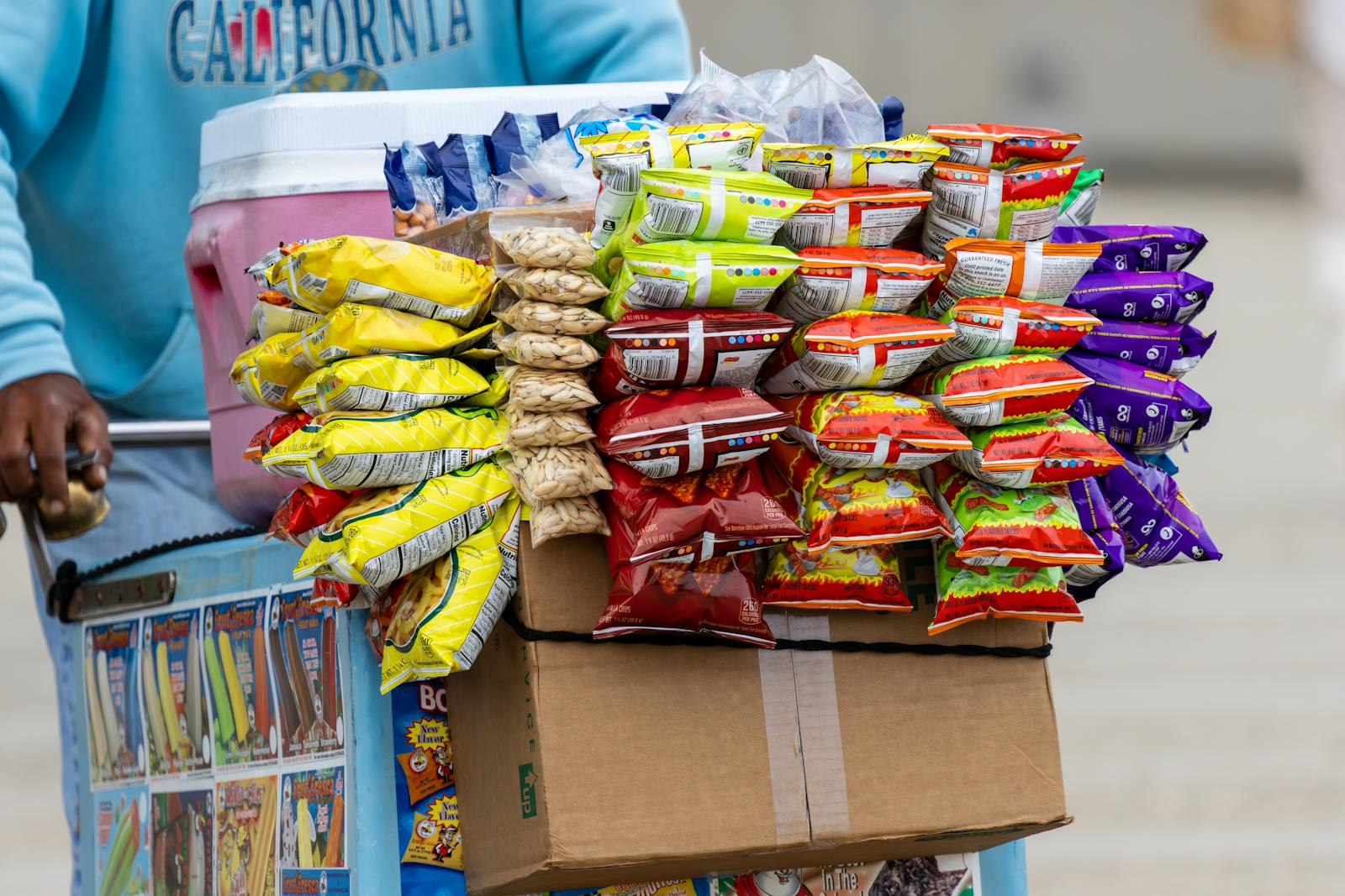 A street vendor's cart filled with a variety of colorful snack packets for sale outdoors.