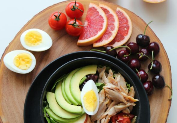 A vibrant, healthy salad bowl with avocado, eggs, tomatoes, grapefruit, and cherries on a wooden board.